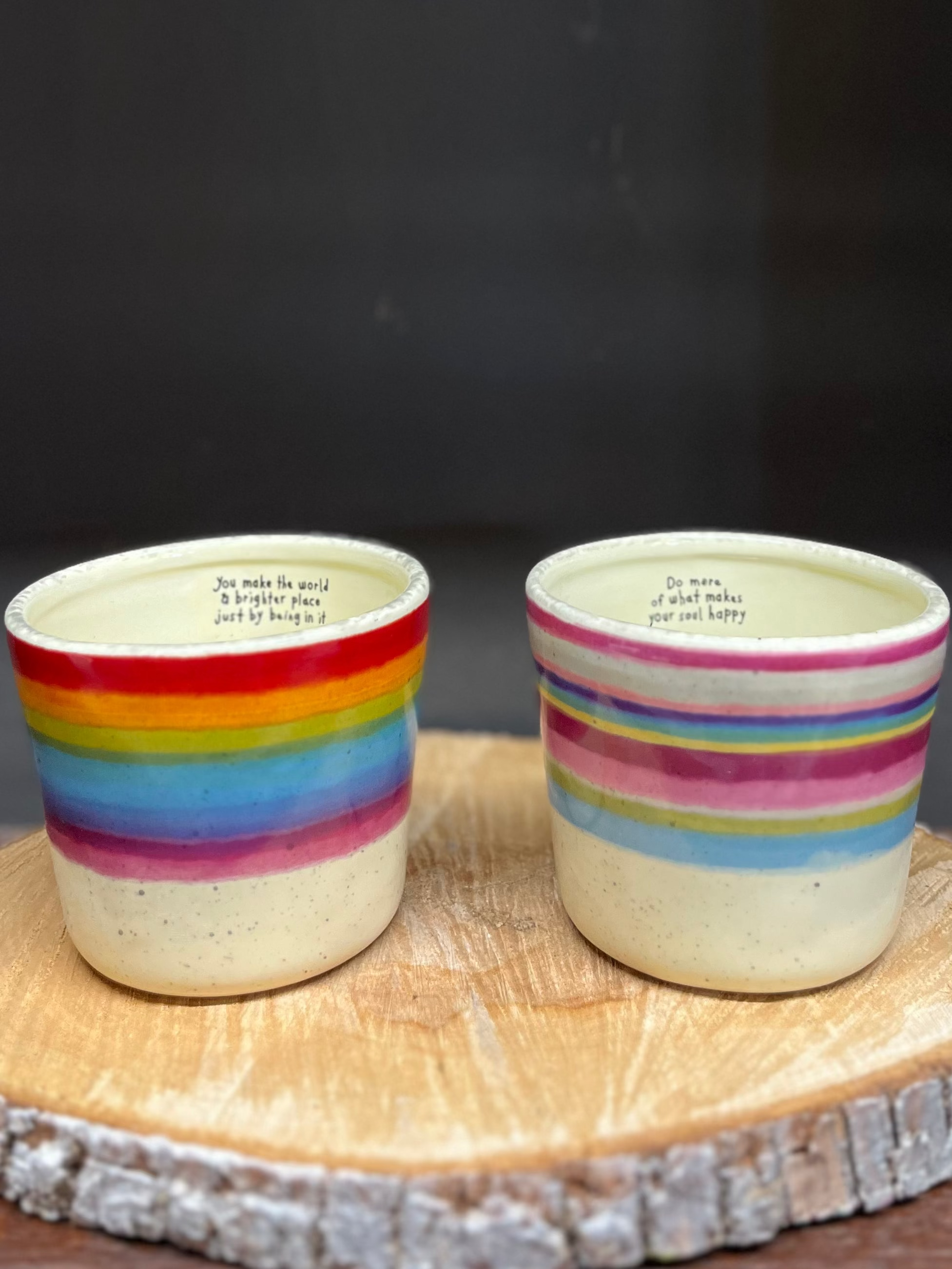 Two ceramic cups with rainbow stripes on a wooden stand against a dark background