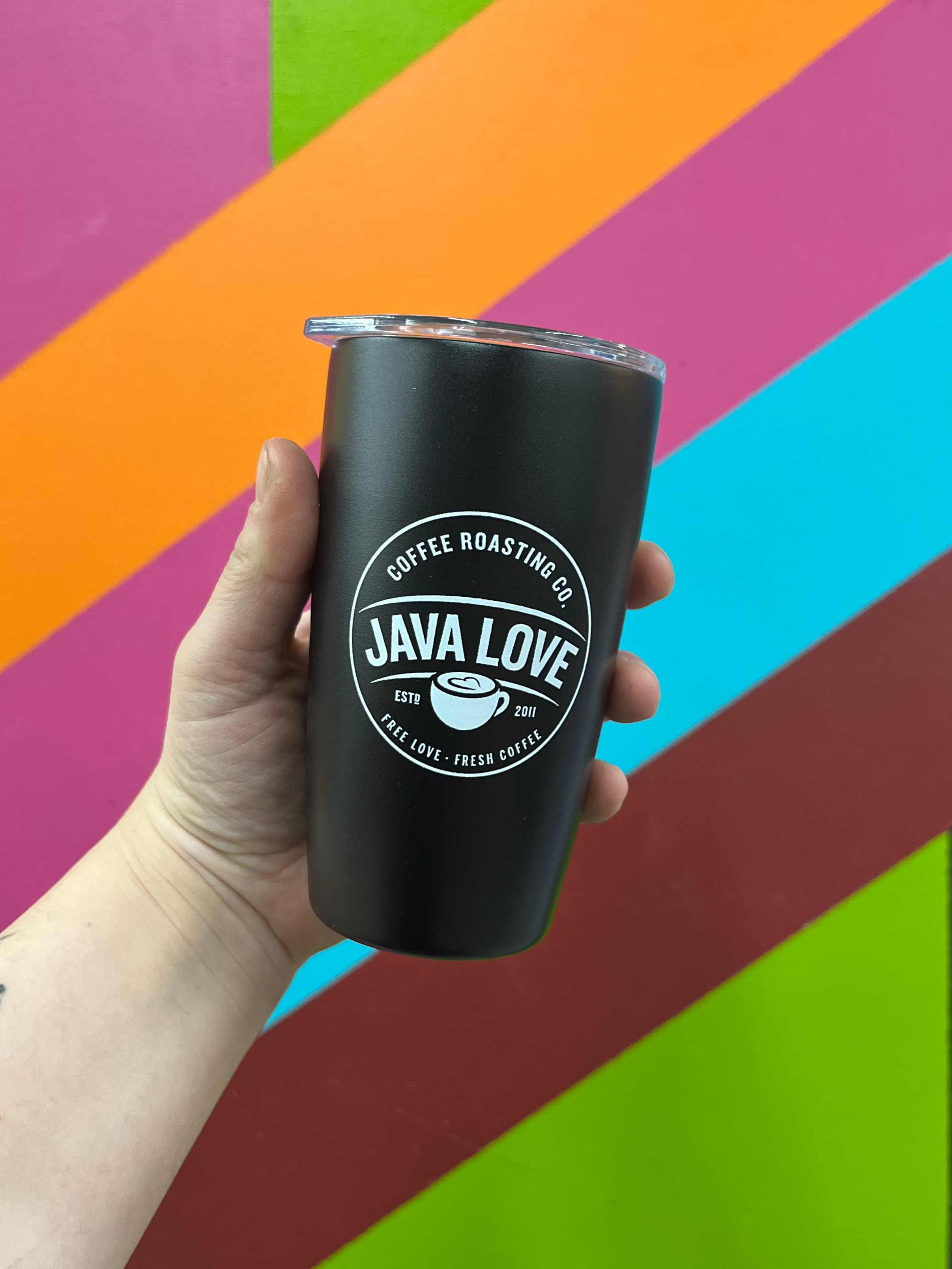 Black tumbler with 'Java Love' logo held against a colorful geometric background