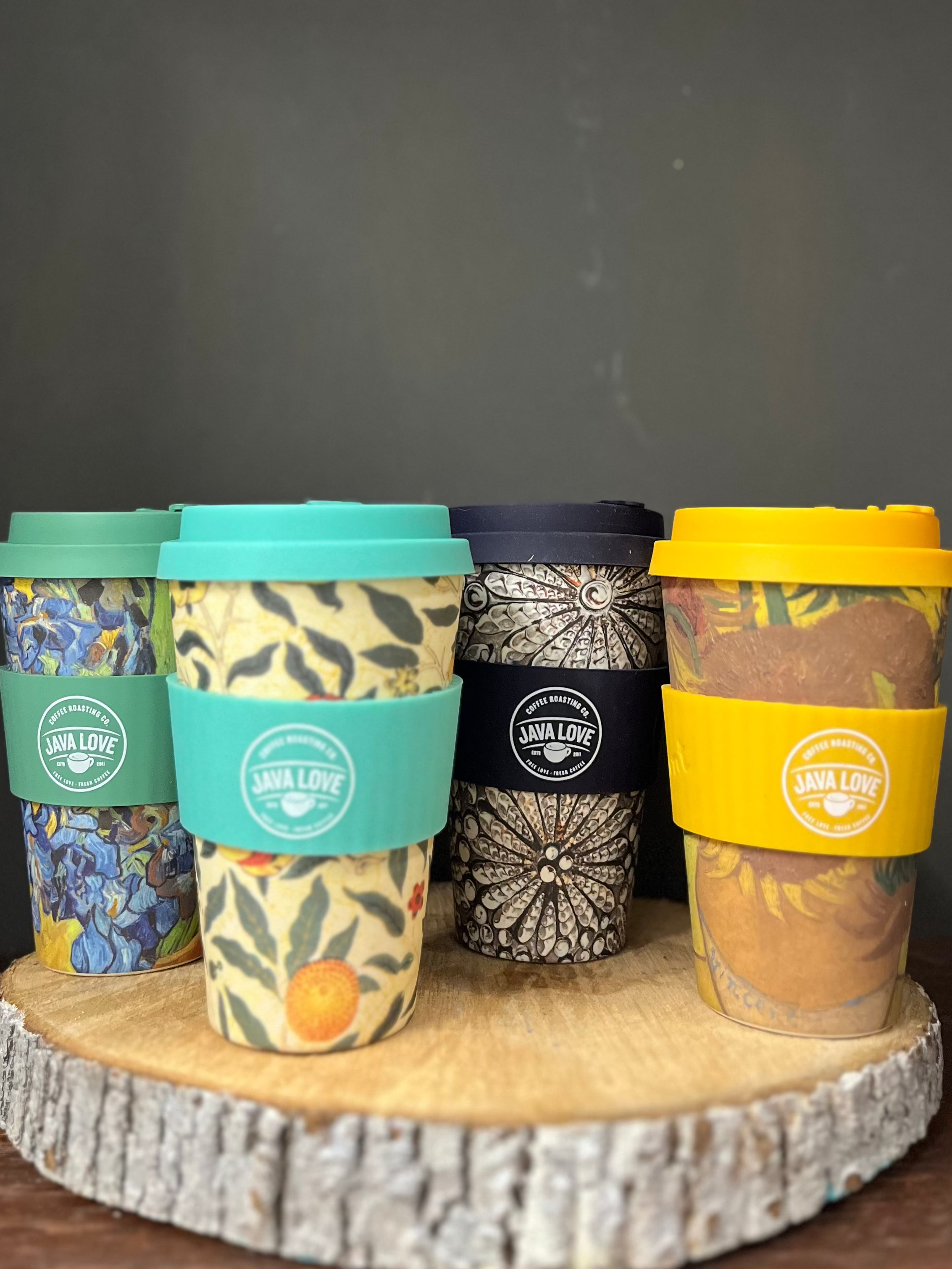 Set of four reusable coffee cups with colorful lids on a wooden stand against a dark background